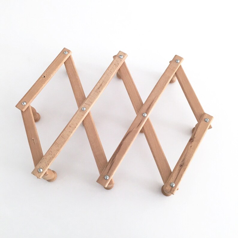 May include: A wooden magazine rack with a foldable design. The rack is made of light brown wood and has a natural finish. It is held together with silver metal rivets.