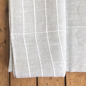 May include: A gray and white striped fabric with a subtle texture. The fabric is folded in half and the edges are visible.
