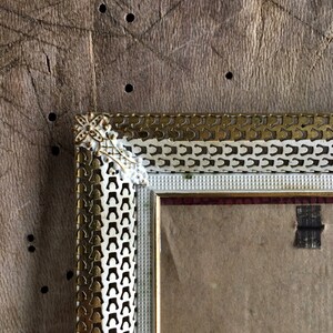 May include: A gold and white picture frame with a decorative design. The frame has a white mount and a clear glass front.
