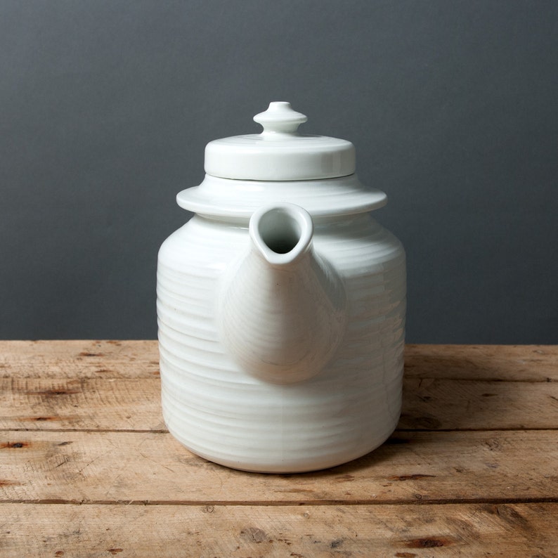 May include: A white ceramic teapot with a rounded body and a lid with a knob on top. The teapot has a spout and a handle.