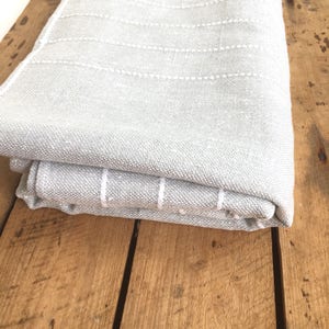 May include: A gray throw blanket with white stripes. The blanket is folded and lying on a wooden surface.