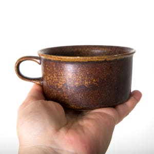 May include: A brown ceramic mug with a speckled glaze. The mug has a rounded shape and a handle.