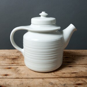 May include: White ceramic teapot with a lid and a handle. The teapot has a textured, ribbed design.