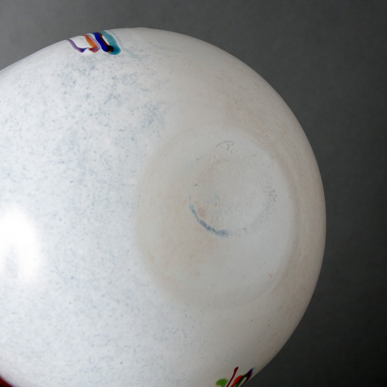 May include: White glass vase with a blue, red, green, and yellow stripe design. The bottom of the vase has a blue signature.