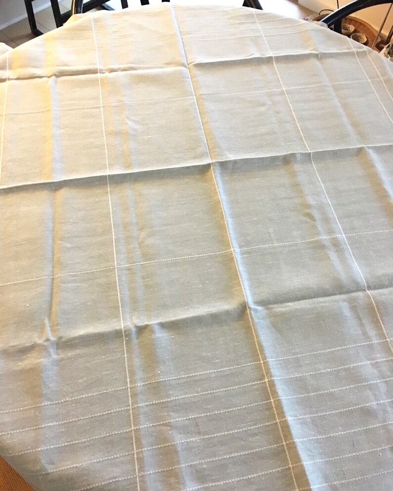 May include: A light gray tablecloth with a subtle white grid pattern. The tablecloth is made of a woven fabric with a slightly textured surface.