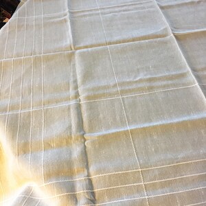 May include: A beige tablecloth with a white checkered pattern. The tablecloth is made of a linen-like material and has a slightly wrinkled texture.