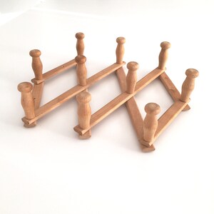 May include: A wooden coat rack with eight hooks, folded in a zig-zag pattern. The rack is made of light brown wood and has a rustic look.