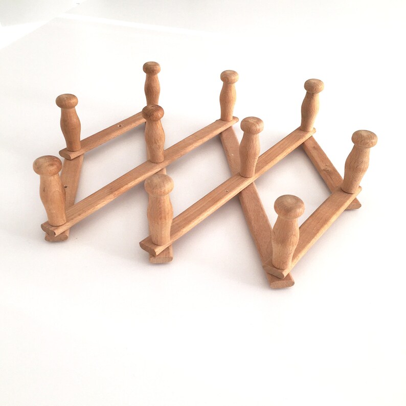 May include: A wooden coat rack with eight hooks, folded in a zig-zag pattern. The rack is made of light brown wood and has a rustic look.