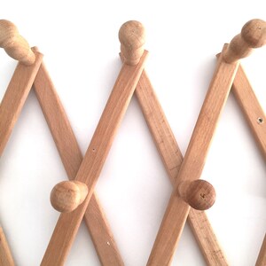 May include: A wooden coat rack with a diamond pattern and multiple hooks. The rack is made of light brown wood and is mounted on a white wall.