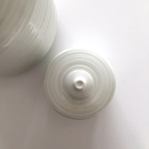 May include: White ceramic lid with a circular design and a small knob on top.