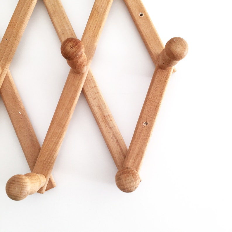 May include: A wooden coat rack with a folding design and multiple hooks. The rack is made of light brown wood and has a natural finish.