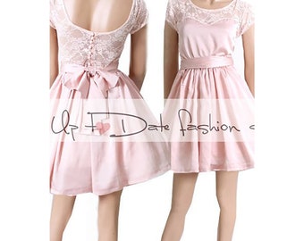 Peut inclure: Une robe en satin rose avec une superposition de dentelle et un nœud à la taille. La robe a des manches courtes et un décolleté arrondi.