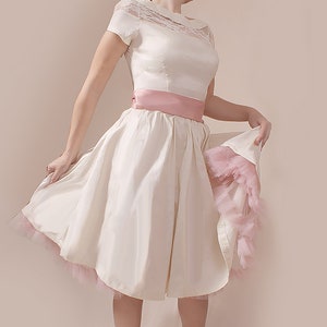 May include: A white satin dress with a lace bodice and a pink satin sash. The dress has a full skirt and a pink tulle underskirt.