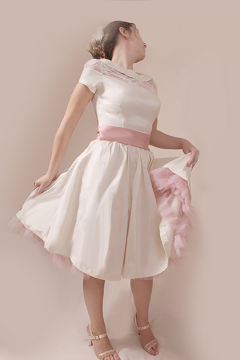 May include: A white satin dress with a lace bodice and a pink satin sash. The dress has a full skirt and a pink tulle underskirt.