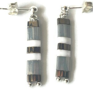 Puede incluir: Un par de pendientes colgantes de plata con un diseño a rayas gris y blanco. Los pendientes están hechos de metal y tienen un estilo simple y elegante.