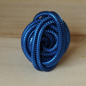 Op de afbeelding: Een close-up van een blauwe kabel die tot een bal is opgerold. De kabel heeft een textuur en is gemaakt van een zacht, flexibel materiaal.
