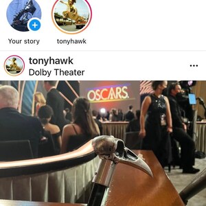 May include: A silver skull-shaped cane with a black handle. The cane is resting on a wooden table in front of a group of people sitting in chairs. The word "OSCARS" is visible in the background.