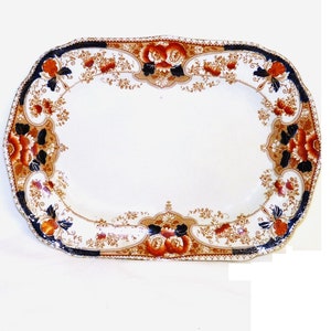 May include: Rectangular white ceramic serving platter with a decorative floral border in orange, navy blue, and gold. The platter has a scalloped edge and is suitable for serving food.