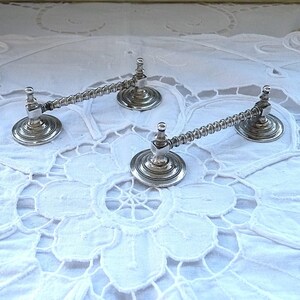 May include: Three silver-toned metal candle holders with a twisted design. The holders are on a white lace tablecloth.