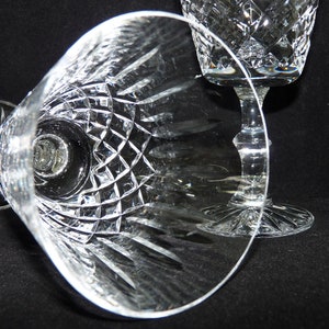 May include: Two clear crystal wine glasses with a cut glass design. The glasses are on a black background.