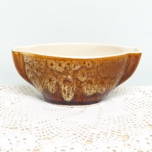 May include: A brown and white ceramic gravy boat with a speckled glaze.