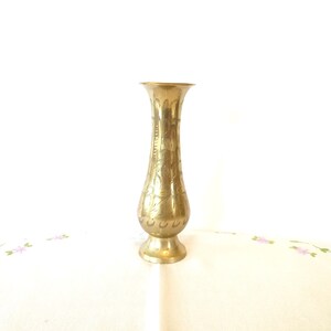 May include: A gold brass vase with an intricate floral design. The vase has a narrow neck and a wide base.