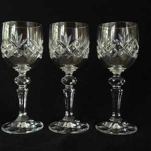 May include: Three clear crystal wine glasses with a cut glass design. The glasses have a round bowl and a long stem.