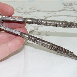 May include: A vintage silver nutcracker with a decorative pattern on the handles. The nutcracker is open and ready to crack nuts.
