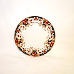 May include: A white ceramic plate with a decorative border featuring a floral pattern in shades of red, orange, gold, and black.