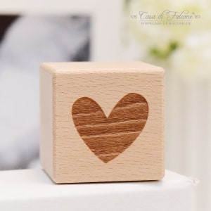 Op de afbeelding: Een houten kubus met een hartvormig ontwerp dat in de voorkant is gegraveerd. Het hart is lichtbruin van kleur en heeft een houtnerfpatroon.
