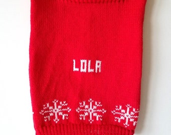 May include: Red knitted Christmas stocking with white snowflakes and the name "LOLA" embroidered on the front.