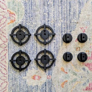 May include: A collection of black plastic parts, including four circular pieces with a cross-shaped design and four smaller, rounded pieces with a slot. The items are arranged on a patterned rug.