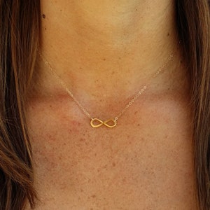 May include: A gold infinity symbol necklace on a delicate chain. The necklace is worn by a person with long brown hair.