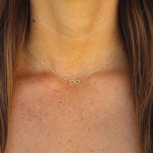Peut inclure: Un collier délicat de couleur dorée doté d'un petit pendentif en forme de symbole de l'infini centré sur une fine chaîne à maillons. Le métal présente une finition polie et le design se compose d'une boucle continue simple autour du cou.