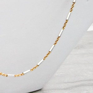 May include: A delicate gold and silver chain necklace with alternating square links. The chain is displayed on a white surface.