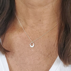Könnte beinhalten: Eine silberne Halskette mit einem einfachen, offenen Kreisanhänger.