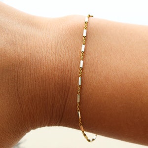 May include: A gold chain bracelet with small rectangular links.