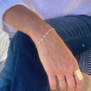 May include: A gold bracelet with small round stones and a gold ring with a textured design. The bracelet and ring are worn on a person's wrist and finger.