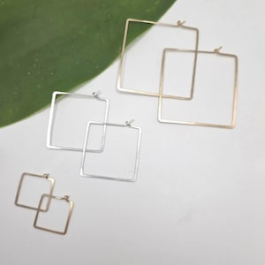 May include: Three pairs of square hoop earrings in varying sizes and metal finishes. One pair is large and gold-toned, one pair is medium and silver-toned, and one pair is small and gold-toned. Each earring features a thin wire frame and a hinged closure.