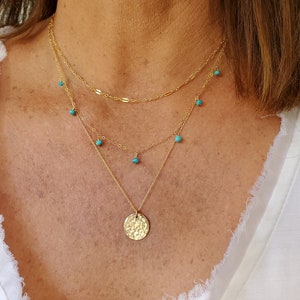 May include: A gold layered necklace with a hammered gold disc pendant and turquoise beads.