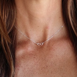 May include: A silver infinity symbol necklace on a silver chain. The necklace is delicate and simple, making it a perfect everyday piece of jewelry.