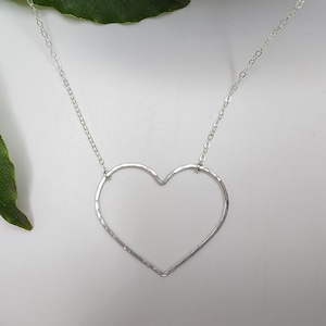 Puede incluir: Un collar de plata con un colgante de coraz&oacute;n abierto martillado. La cadena es delicada y el coraz&oacute;n tiene un dise&ntilde;o simple y moderno.
