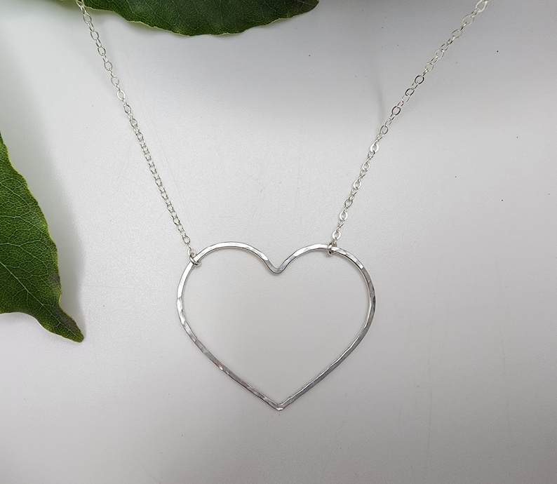 Puede incluir: Un collar de plata con un colgante de coraz&oacute;n abierto martillado. La cadena es delicada y el coraz&oacute;n tiene un dise&ntilde;o simple y moderno.
