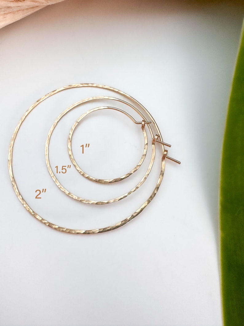 May include: Three gold hoop earrings of different sizes. The smallest hoop is 1 inch in diameter, the middle hoop is 1.5 inches in diameter, and the largest hoop is 2 inches in diameter.