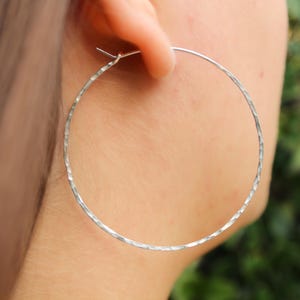 May include: Silver hoop earrings with a textured finish. The earrings are large and circular.