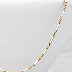 May include: A delicate gold chain necklace with silver bar accents. The chain is thin and has a delicate, feminine look.
