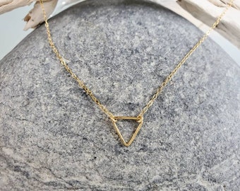 May include: A delicate gold-tone necklace featuring a small, open triangular pendant suspended from a thin, fine-link chain. The metal has a polished, reflective finish, and the geometric charm is centered along the length of the chain.