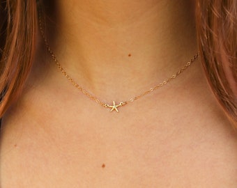 May include: A delicate gold-toned chain necklace featuring a small, centered starfish pendant. The starfish charm is metallic gold in color and is attached directly to the fine link chain, resting horizontally against the base of the neck.