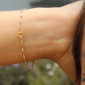 May include: A gold chain bracelet with a small, round clasp. The bracelet is made of thin, linked chains with alternating gold and silver colored links.