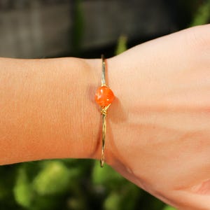 Peut inclure: Un bracelet en fil d'or avec une seule pierre de cornaline orange.